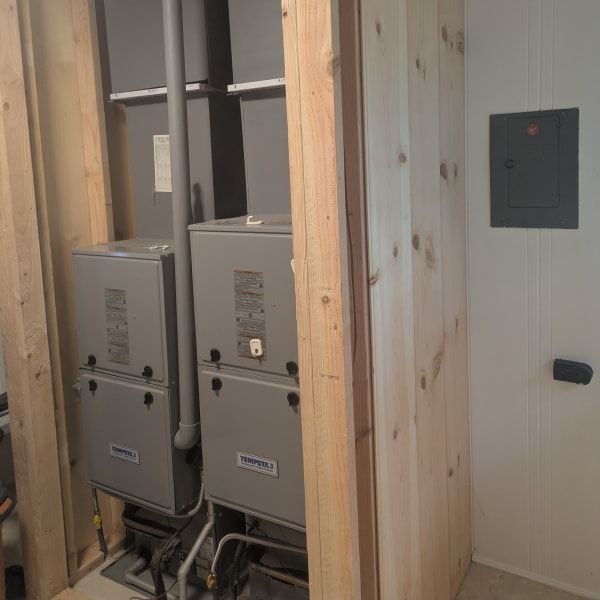 Two gray electrical panels inside a wood-framed wall cavity, with a small wall switch beside them.