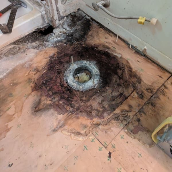 Burned floor around a damaged toilet flange and pipe opening in a room corner