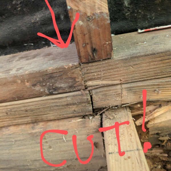 Close-up of a broken wooden beam joint with a red arrow and “CUT!” written in marker.