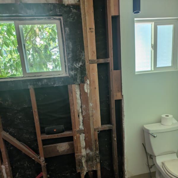Bathroom under renovation with exposed studs, window, and a toilet beside a partially finished wall