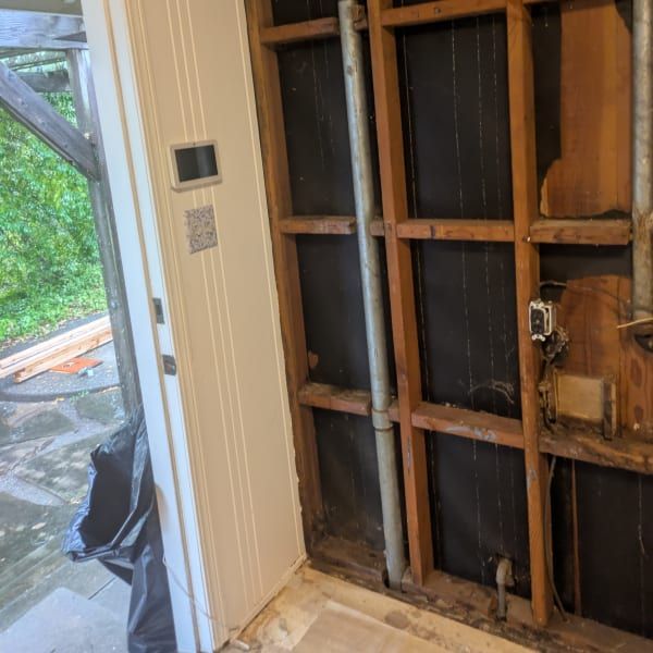 Damaged interior wall with exposed studs beside a glass door and outdoor deck view