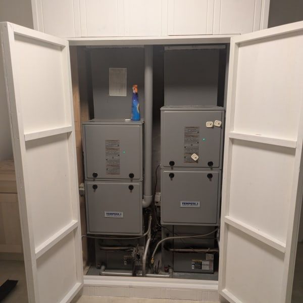 Open white closet doors revealing two gray utility units and cabinets inside a wall niche.