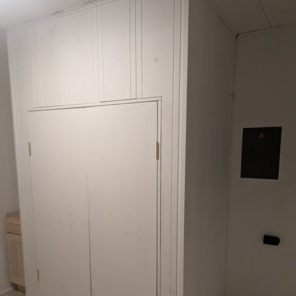 White paneled closet door in a narrow hallway beside a wall-mounted black panel.