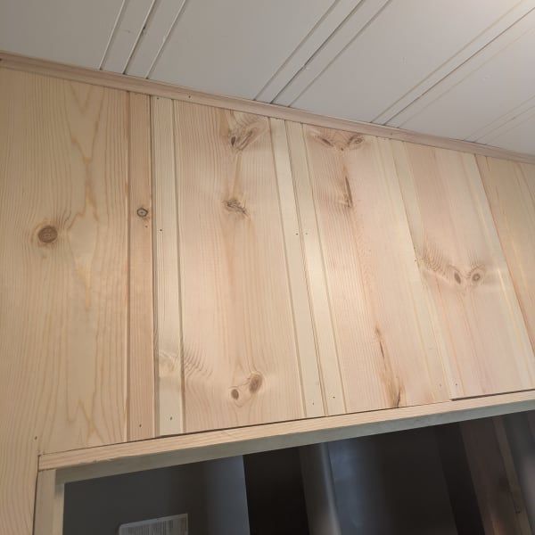 Light wood paneling above a doorway, with a white paneled ceiling and dark opening below