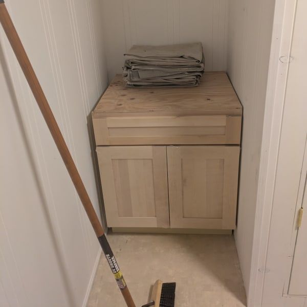 Wooden cabinet in a narrow hallway corner, with folded papers on top and a broom leaning nearby.