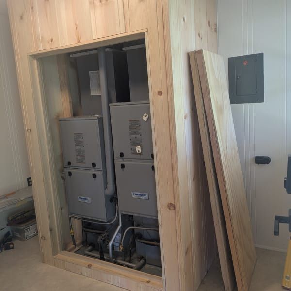 Utility closet with metal HVAC equipment installed in a wooden-framed opening during construction.
