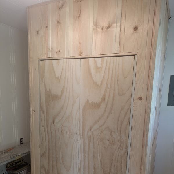Plywood wall covering with a large centered hatch or panel in a small room