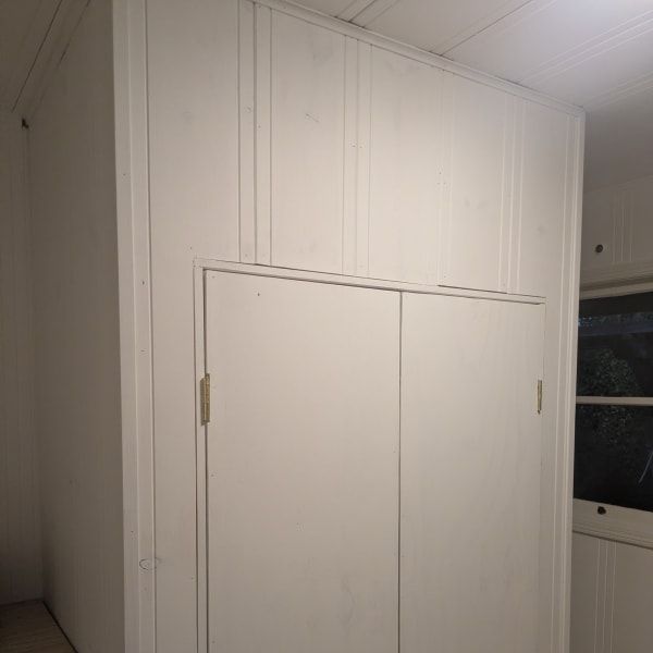 White built-in cabinet with double doors on a wall near a window in a dim room