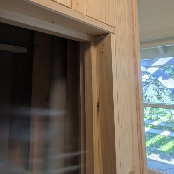 Partially open wooden closet door with a dark interior and a window view of greenery beyond
