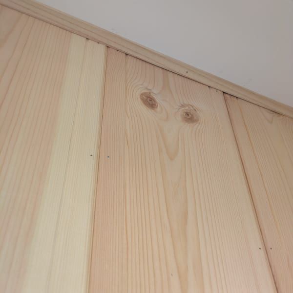 Close-up of light pine wood wall panels with knots and vertical grain under a ceiling trim.