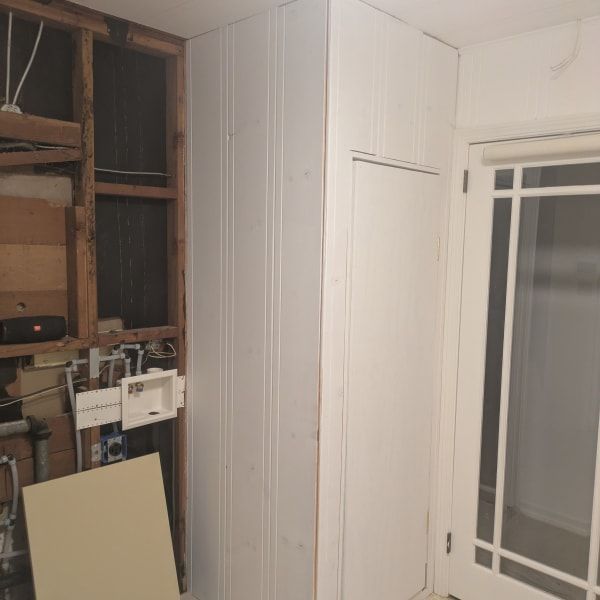 Small unfinished room with exposed wiring, a beige panel leaning against the wall, and a white door or window frame.