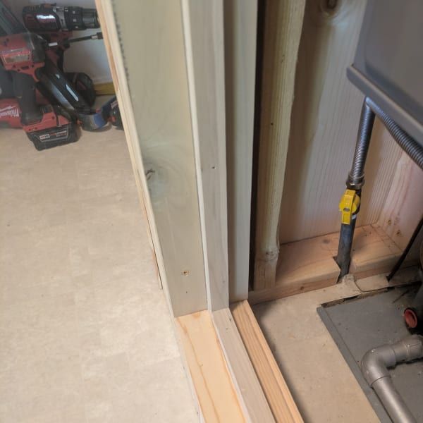 Close-up of a doorway with unfinished trim and exposed framing beside carpet and tools on the floor