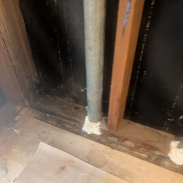 Exposed indoor wall framing with a gray pipe and damaged wood near the floor.