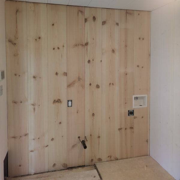 Bare plywood wall with electrical outlets, switches, and a thermostat in an unfinished room