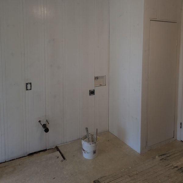 Empty room with white walls, unfinished floor, a bucket of tools, and a closed door.