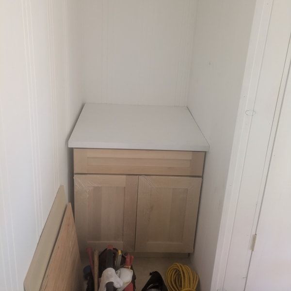 Narrow hallway nook with a light wood cabinet and cleaning items on the floor.
