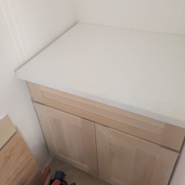 White countertop on a light wood cabinet in a corner against white walls