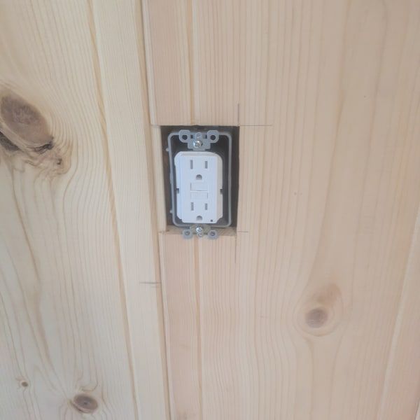 White electrical outlet installed in a pine wood wall with a dark metal box.
