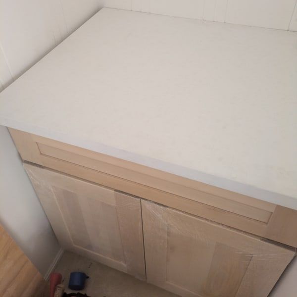 White countertop above light wood cabinet in a corner, with a small blue object on the floor.