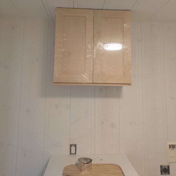 Small kitchen wall with beige cabinets above a countertop and sink opening.