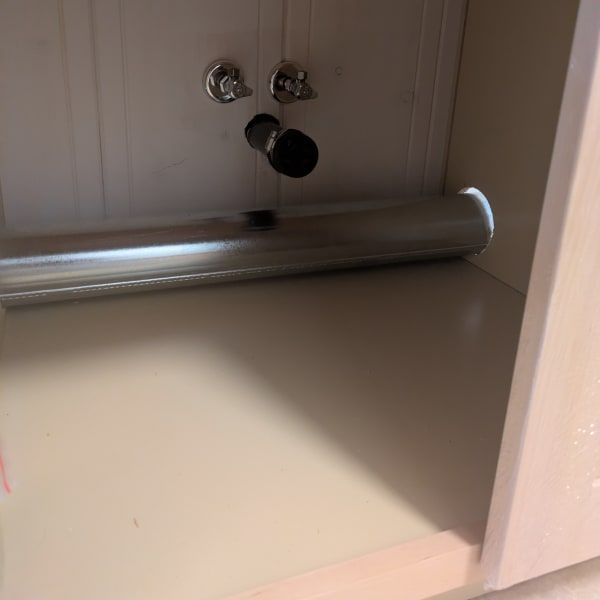 Under-sink cabinet with a chrome pipe and faucet fittings against a beige interior.