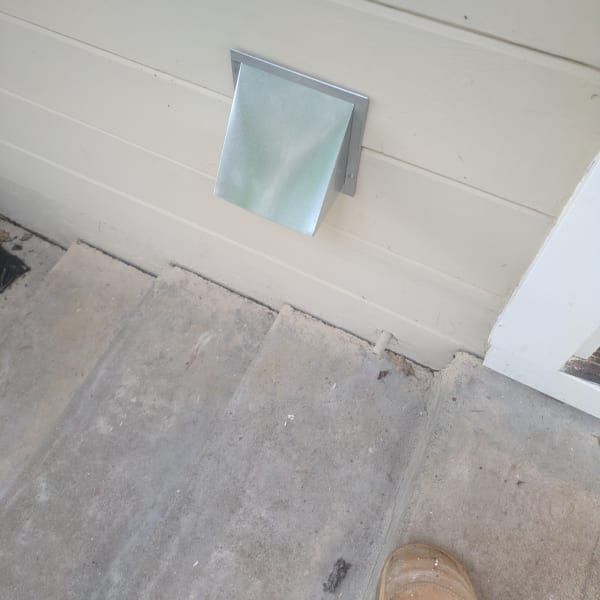 Small metal wall vent above a concrete floor beside a white door.