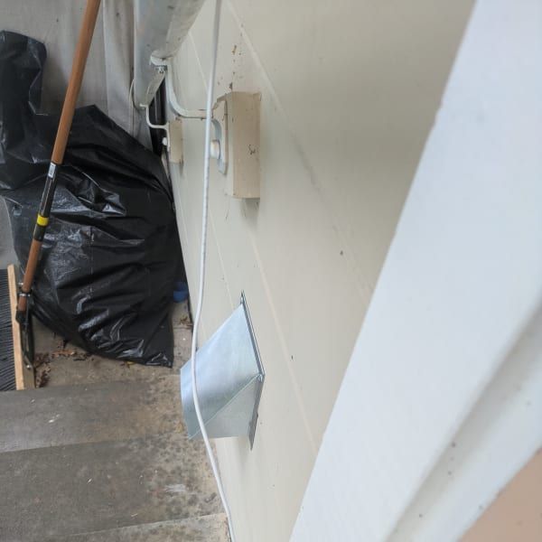 White wall corner with a small vent cover, next to stairs and a black trash bag in a narrow indoor space