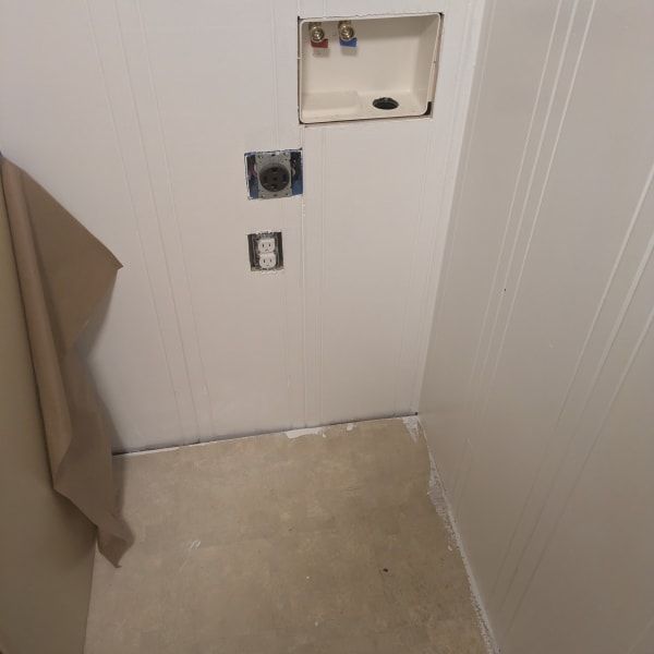 Bathroom wall with recessed plumbing and electrical openings above a bare floor area.