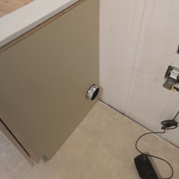 Open beige cabinet door with a round knob beside a wall and floor cord.