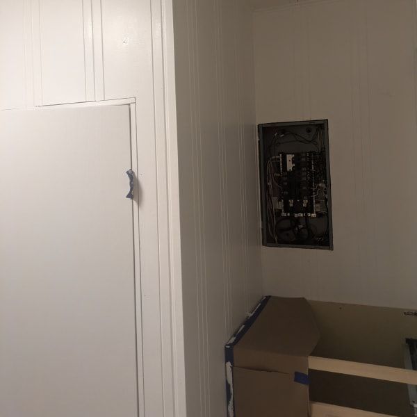 White interior wall with open electrical panel above a cardboard box near a door or cabinet