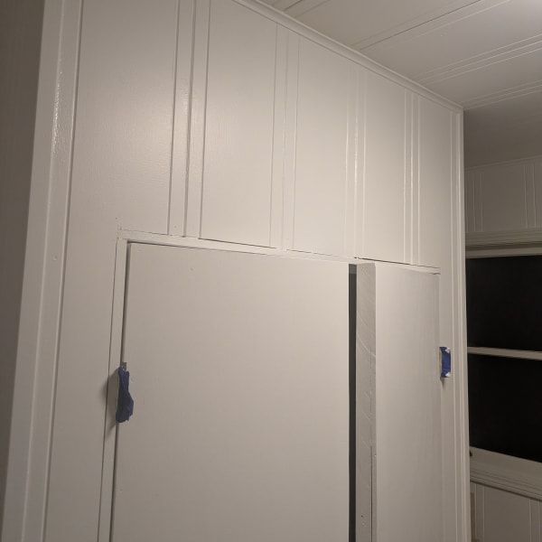 White paneled closet doors with blue tape on a wall in a bright room.