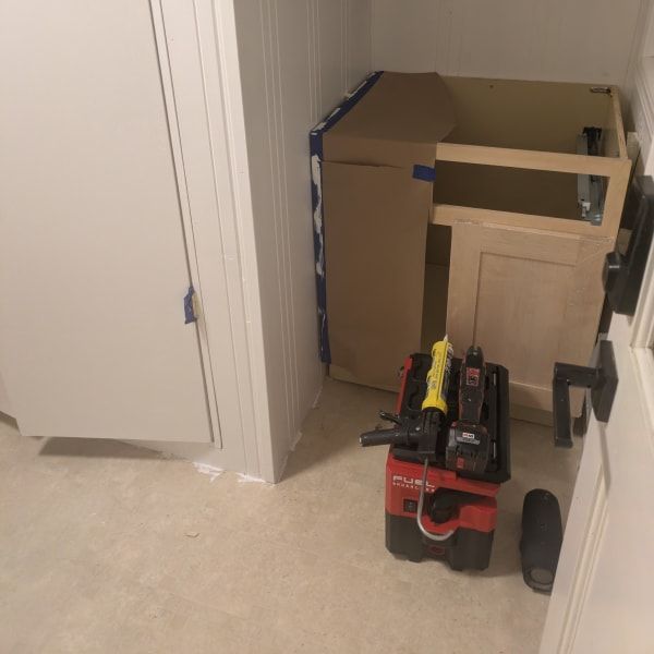 Red tool cart in a hallway beside stacked boxes and furniture, with a white door and carpeted floor.
