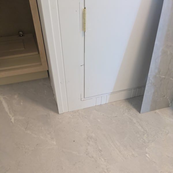White cabinet door beside an open doorway, with a light gray floor and wall paneling.