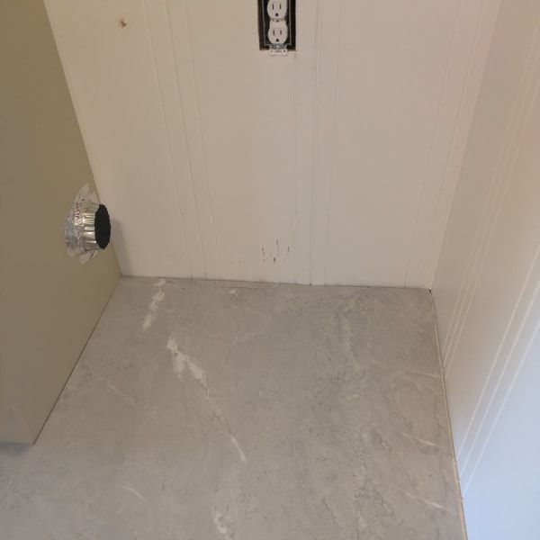 Empty room corner with unfinished gray floor, white walls, and an open door on the left.