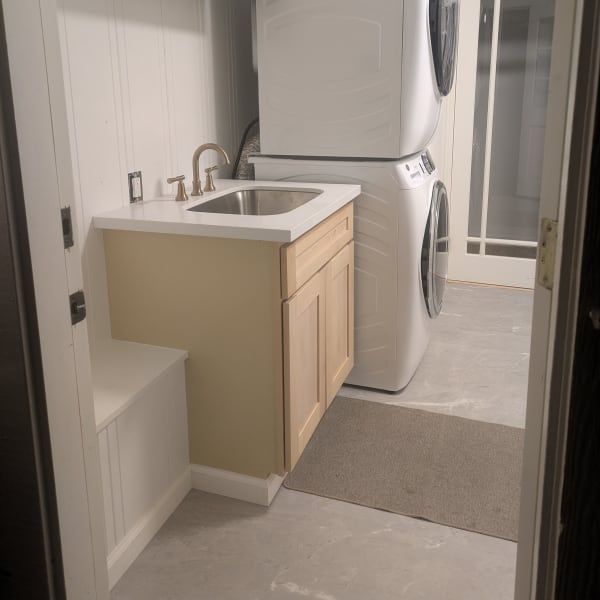 Compact laundry room with stacked washer and dryer beside a small sink and light wood cabinet.