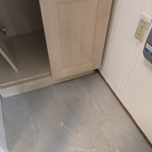 Small bathroom corner with a gray floor, beige cabinet, and white wall with outlet and light switch.