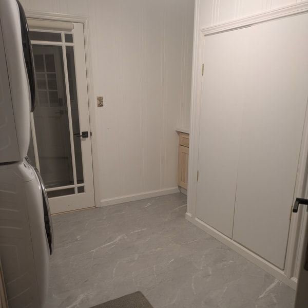 Empty kitchen with gray tile floor, white walls, and a glass door leading outside