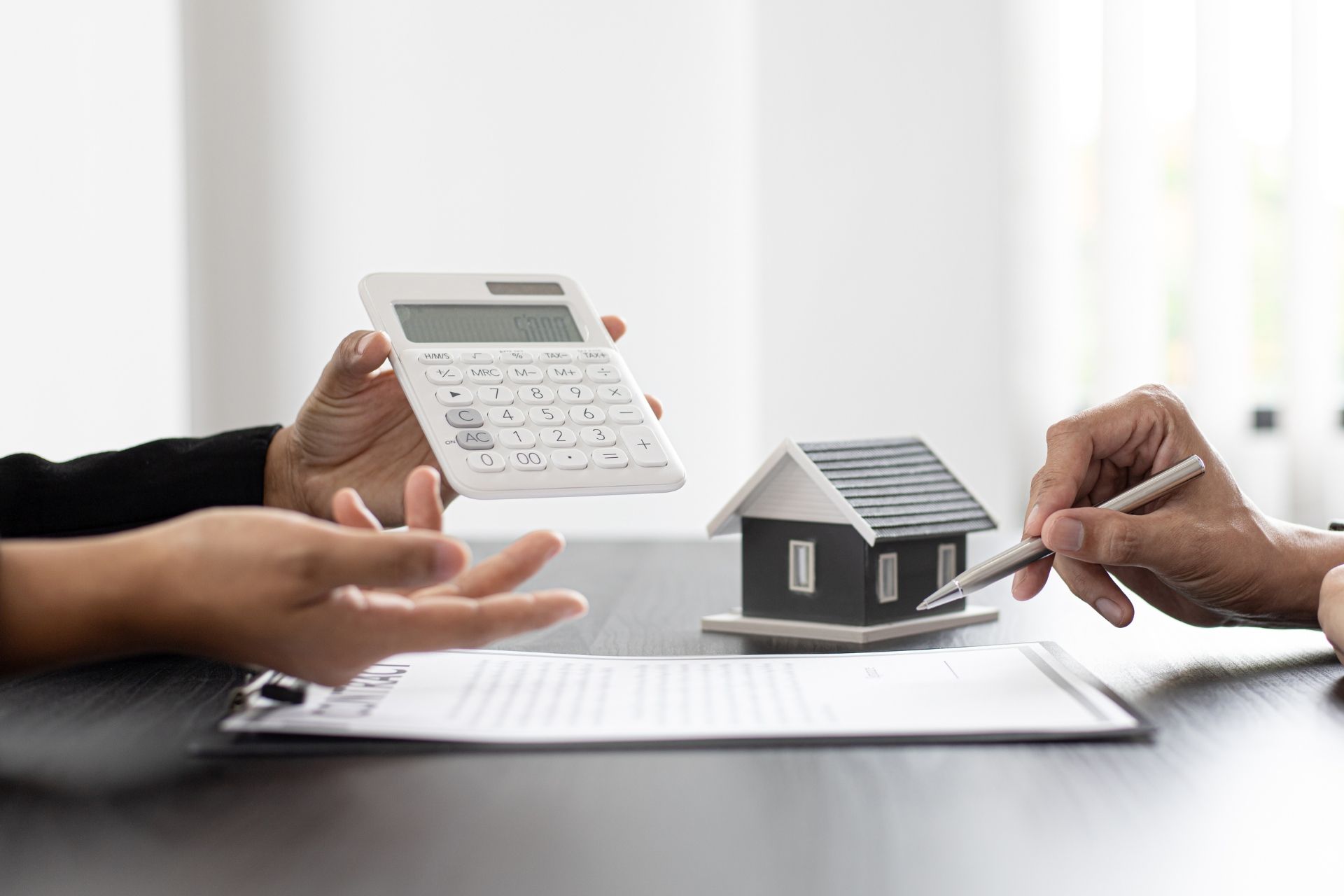 Hands, calculator, and house model over paperwork, illustrating calculation.