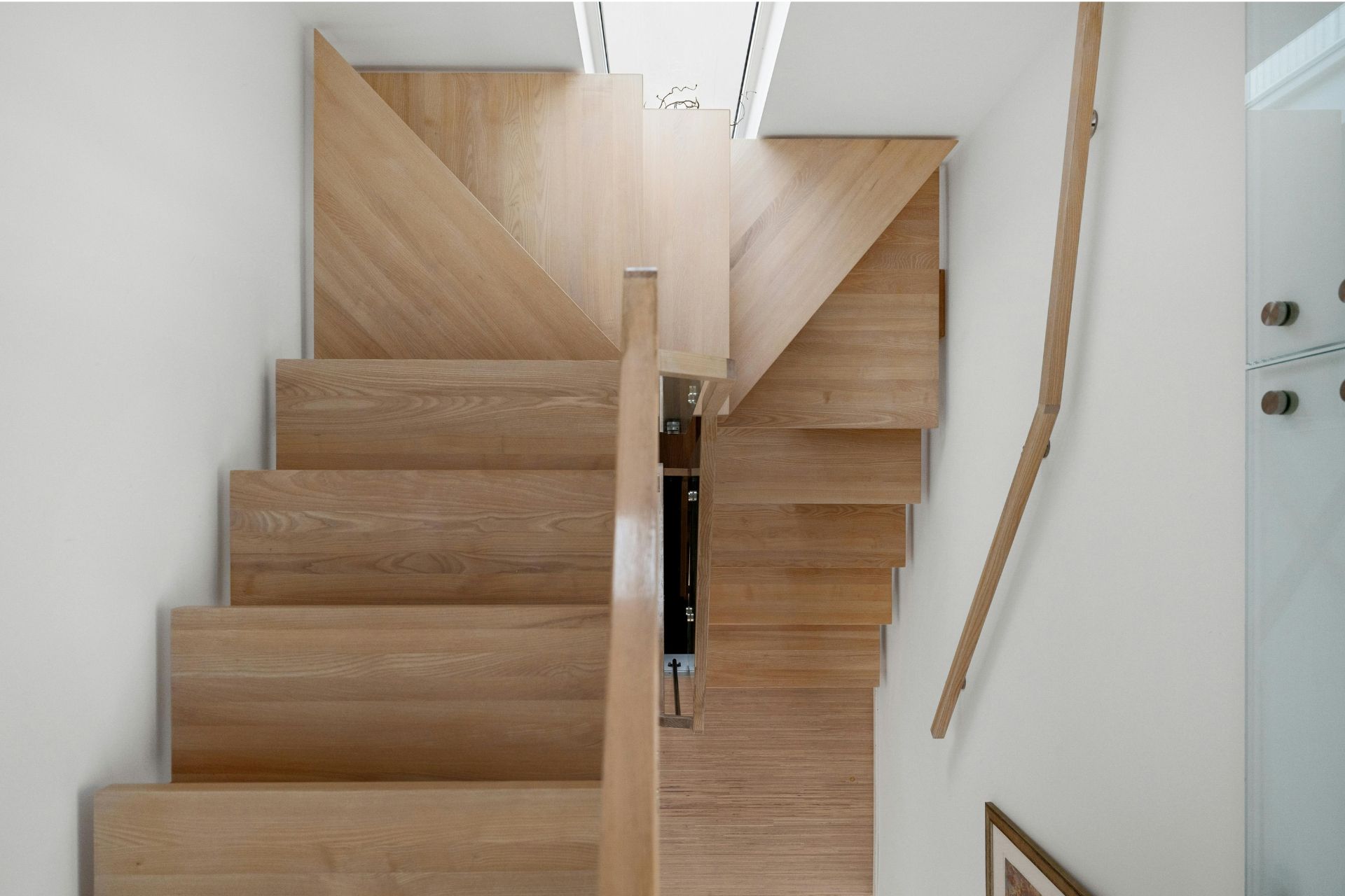 Wooden staircase with open treads and a central gap, viewed from above in a bright white interior.