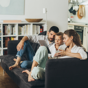 Family sitting on a couch, looking at a tablet together in a cozy living room
