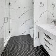 Modern white bathroom with marble walls, black herringbone floor, shower, toilet, and vanity sink