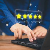 Hand using a laptop with glowing five-star rating icons above the keyboard