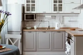 Bright white kitchen with gray cabinets, wood countertops, tiled backsplash, and a small dining table