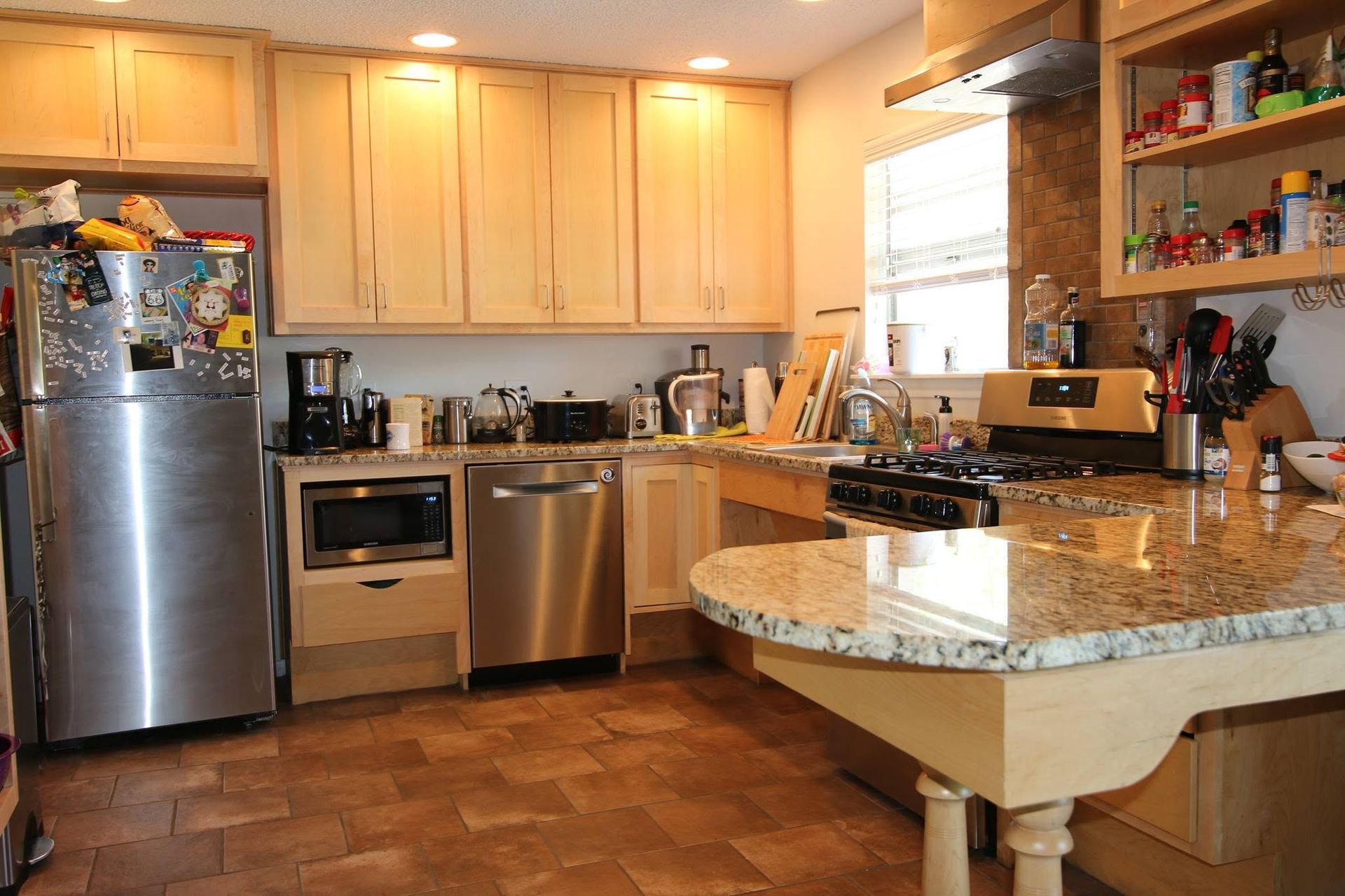 Modern kitchen with stainless steel appliances, light wood cabinets, and a granite island counter