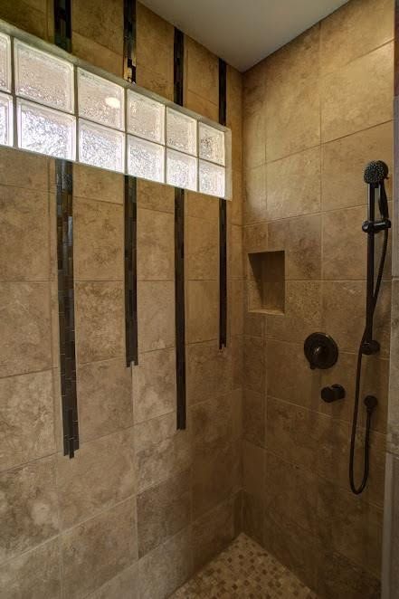 Tile shower with frosted glass block window and dark wood accents, featuring a handheld showerhead.