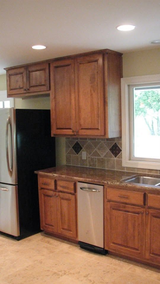 Kitchen with wood cabinets, stainless refrigerator, tiled backsplash, and a window over the sink.