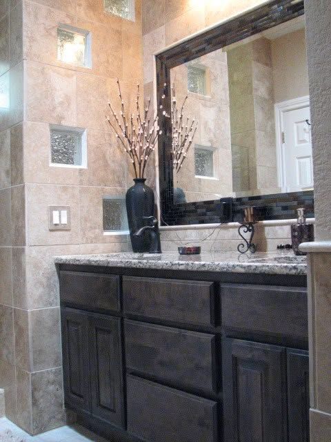 Bathroom vanity with dark wood cabinets, stone countertop, large mirror, and beige tiled walls.