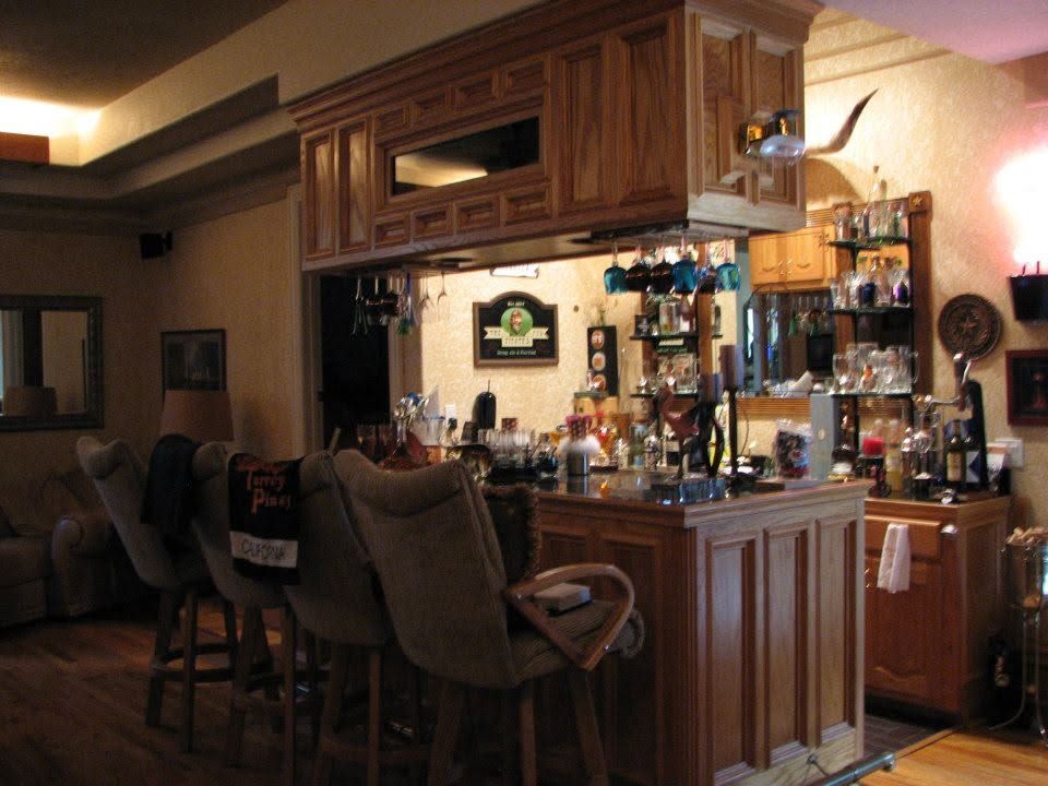 Wood-paneled home bar with stools, bottles, and glassware in a warm-lit room