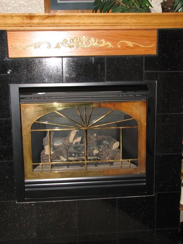 Black-tiled fireplace with a brass-screen insert and carved wooden mantel shelf above