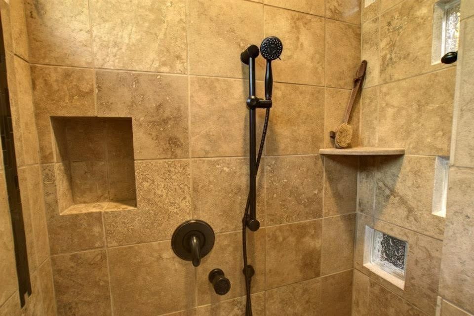 Walk-in shower with beige tile, black showerhead, built-in niches, and a handheld sprayer.